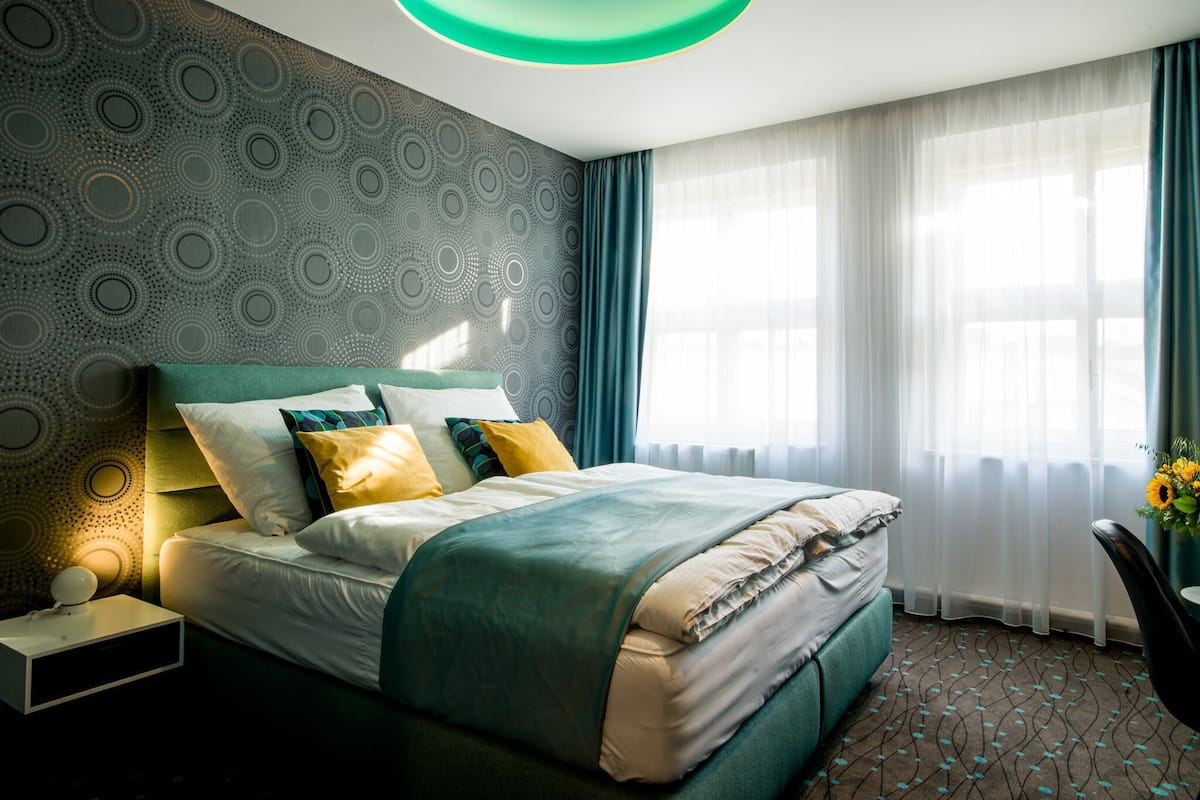 A modern bedroom with a bed, a bedside table, a lamp, and a window with curtains.