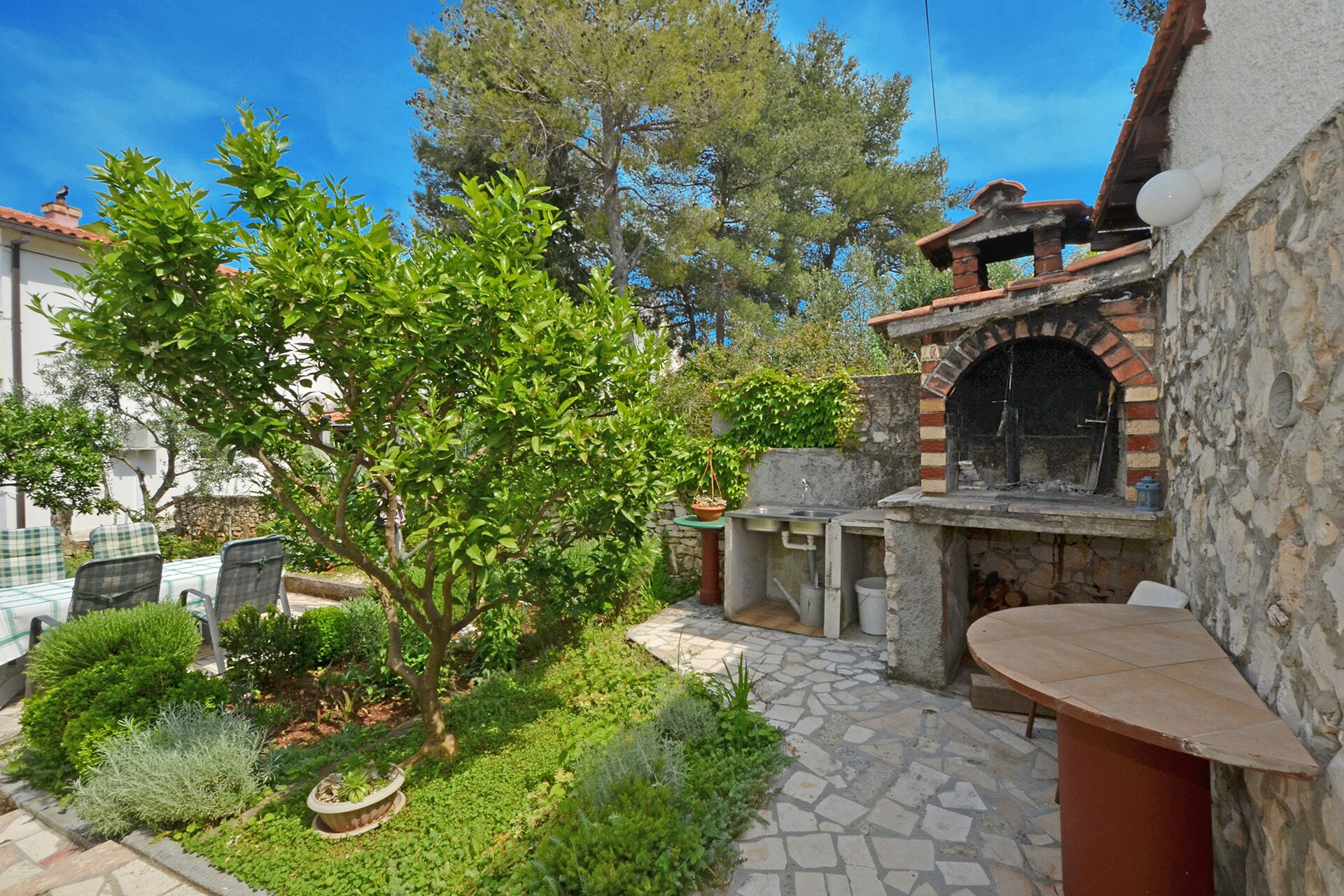 A courtyard with a stone pathway, a small tree, and a brick oven.