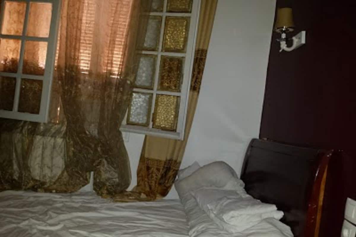 A bed with white bedding, a window with curtains, and a wall-mounted lamp.