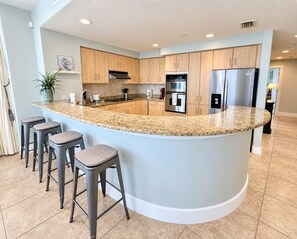 A modern kitchen with a central island, bar stools, stainless steel appliances, and light blue cabinetry. - 🌴Things are different at the beach! It's relaxing season all year long.🚤🐬 (Gulf Shores)