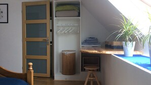 A room with a sloped ceiling, a wooden bed, a wardrobe with a mirror, a small stool, and a window with a plant. - Ti Anna Breizh cottage label 4 * (Lannilis)