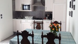 A modern kitchen with white cabinets, a microwave, and a stove. There is a dining table with a blue tablecloth and a vase of flowers. - Ti Anna Breizh cottage label 4 * (Lannilis)