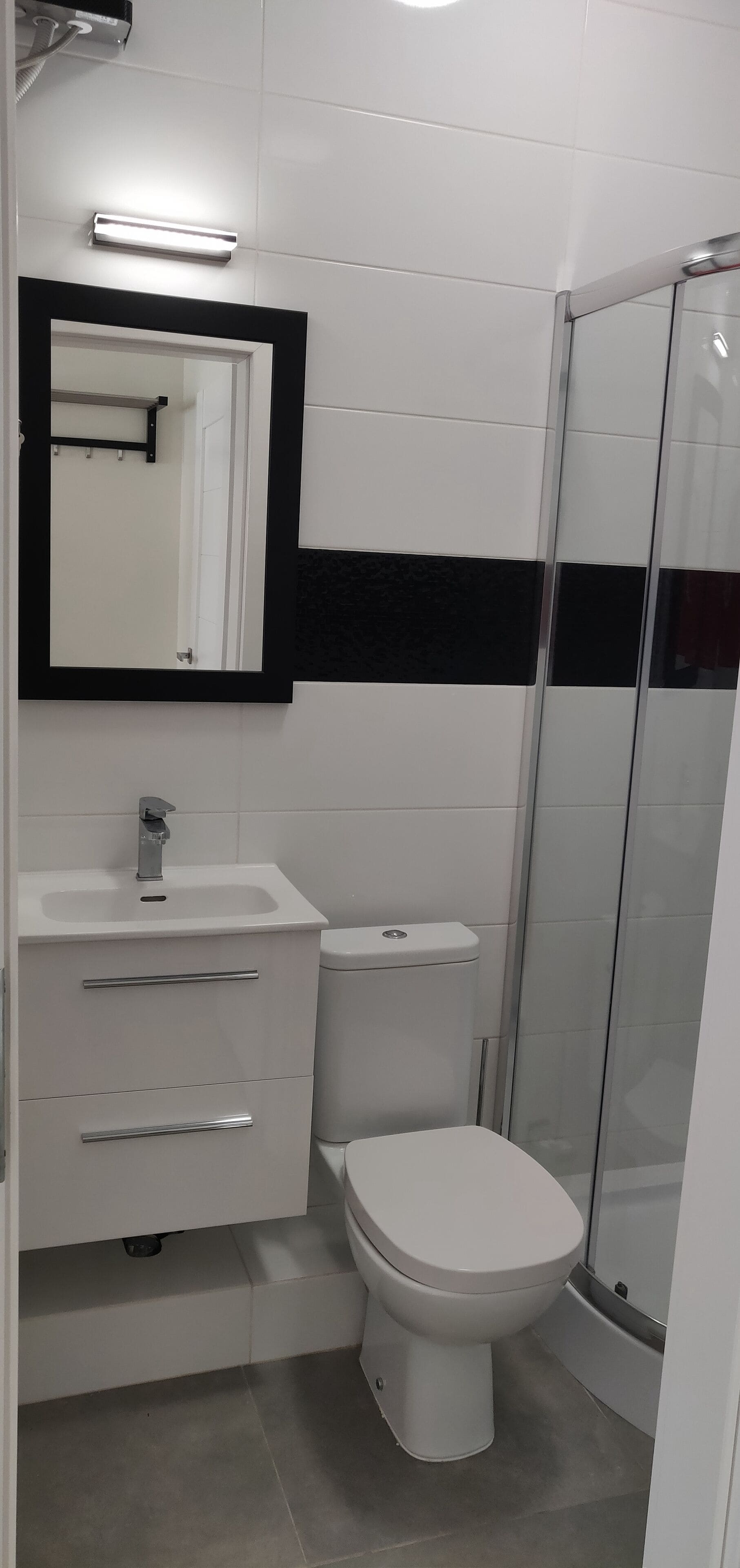 A modern bathroom with a white sink, a toilet, a mirror, and a glass shower enclosure.