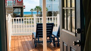 Une terrasse en bois avec des chaises, une clôture blanche et une vue sur les bâtiments et l’océan.