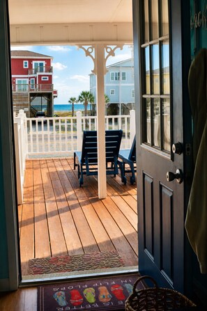 A wooden deck with chairs, a white fence, and a view of buildings and the ocean.