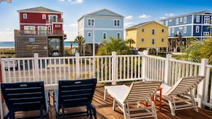 Une terrasse en bois avec des meubles d’extérieur, une clôture blanche et, au fond, des maisons aux couleurs vives.