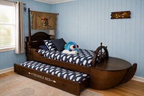 A nautical-themed bedroom with a trundle bed, a ship wheel, and a skull and crossbones flag.