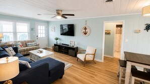Un salon comprenant un canapé, un téléviseur, un ventilateur de plafond et un coin repas avec une table et des chaises.