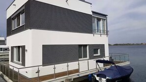 Un edificio moderno de dos pisos frente al agua, con un muelle y un barco.