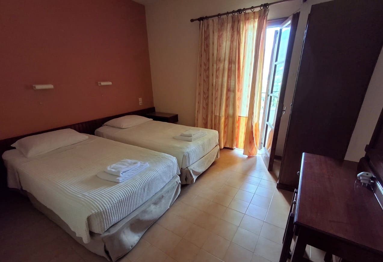 Een hotelkamer met twee bedden, een houten bureau en een raam met gordijnen.
