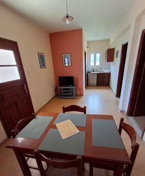 A dining area with a table and chairs, a television, and a kitchen in the background. - Margarita Apartments (Corfu)
