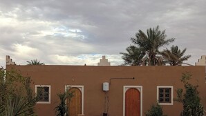 Un patio con un sendero de tierra, palmeras y un edificio con dos puertas y ventanas de madera.