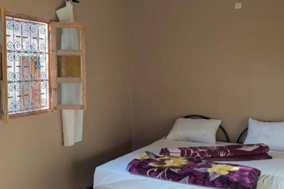 A bedroom with a bed, pillows, a window with metal bars, and a wooden shelf.