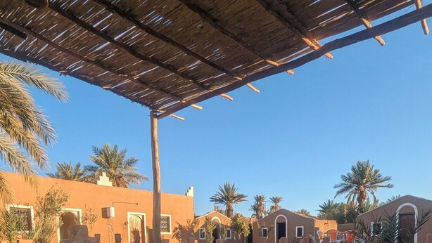 Un espacio al aire libre con mobiliario tradicional, cojines estampados y una estructura de techo de paja.