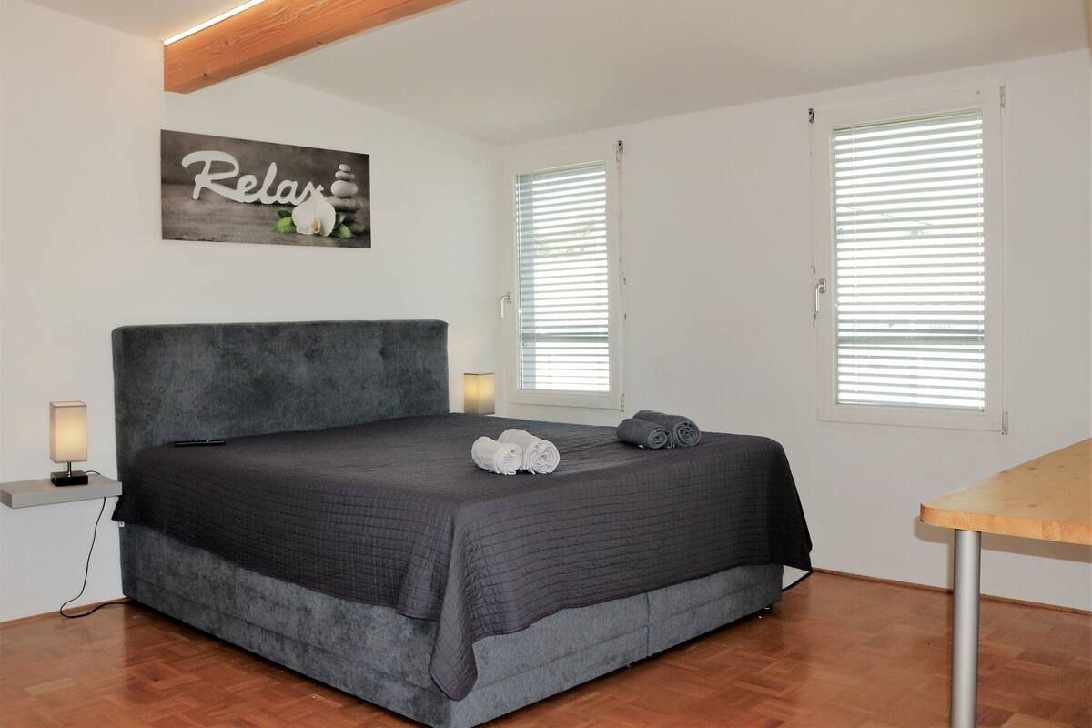 A bedroom with a large bed, two bedside tables with lamps, a wooden ceiling, and a wall-mounted artwork.