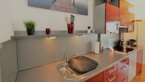 Een moderne keuken met een inbouwspoelbak, een magnetron en een koffieapparaat. Op de muur hangt een schilderij van een pier en op het aanrecht staat een potplant.