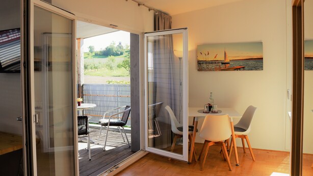 Een kamer met een schuifglazen deur die leidt naar een terras buiten met een tafel en stoelen.