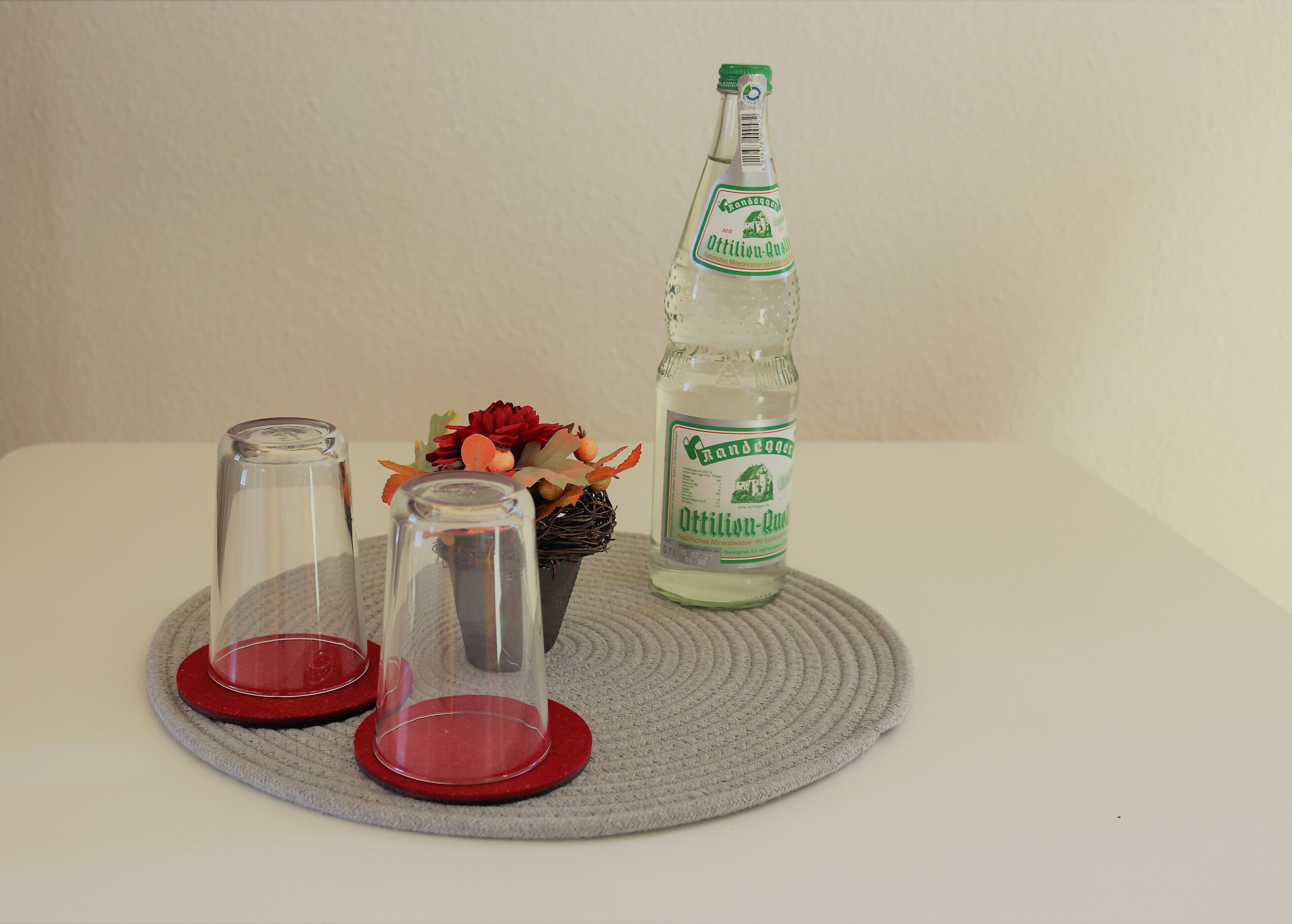 A bottle of Oettinger beer, two clear glasses, and a decorative arrangement on a woven mat.