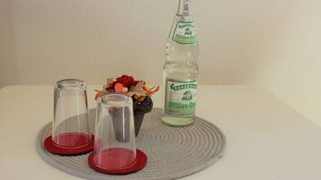 A bottle of Oettinger beer, two clear glasses, and a decorative arrangement on a woven mat.