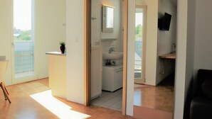 Een moderne, open woonruimte met een keuken, een badkamer met spiegel en wastafel, en een zithoek met televisie.