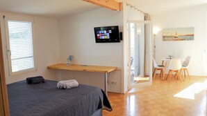 Een slaapkamer met een bed, een televisie, een bureau en een zithoek met stoelen.