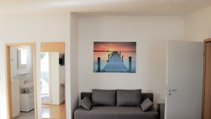 Een moderne woonkamer met een grijze bank, een houten vloer en een schilderij van een zonsondergang boven een steiger.
