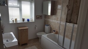 A bathroom with a bathtub, toilet, sink, and window with blinds. - B&B By The Sea (Lymington)