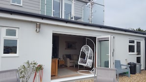 A modern house with a large open door leading to a living room with a sofa, a hanging chair, and a small table. - B&B By The Sea (Lymington)