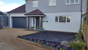 A two-story house with a grey exterior, a dark garage door, and a number '60' on the wall. - B&B By The Sea (Lymington)