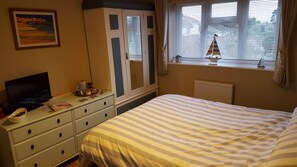 A bedroom with a bed, a dresser, a television, a window with blinds, and a painting on the wall. - B&B By The Sea (Lymington)