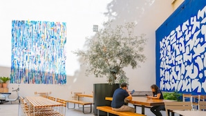 An outdoor seating area with wooden tables and benches, a potted plant, and a wall with abstract art. - The People - Marseille - Hostel (Marseille)