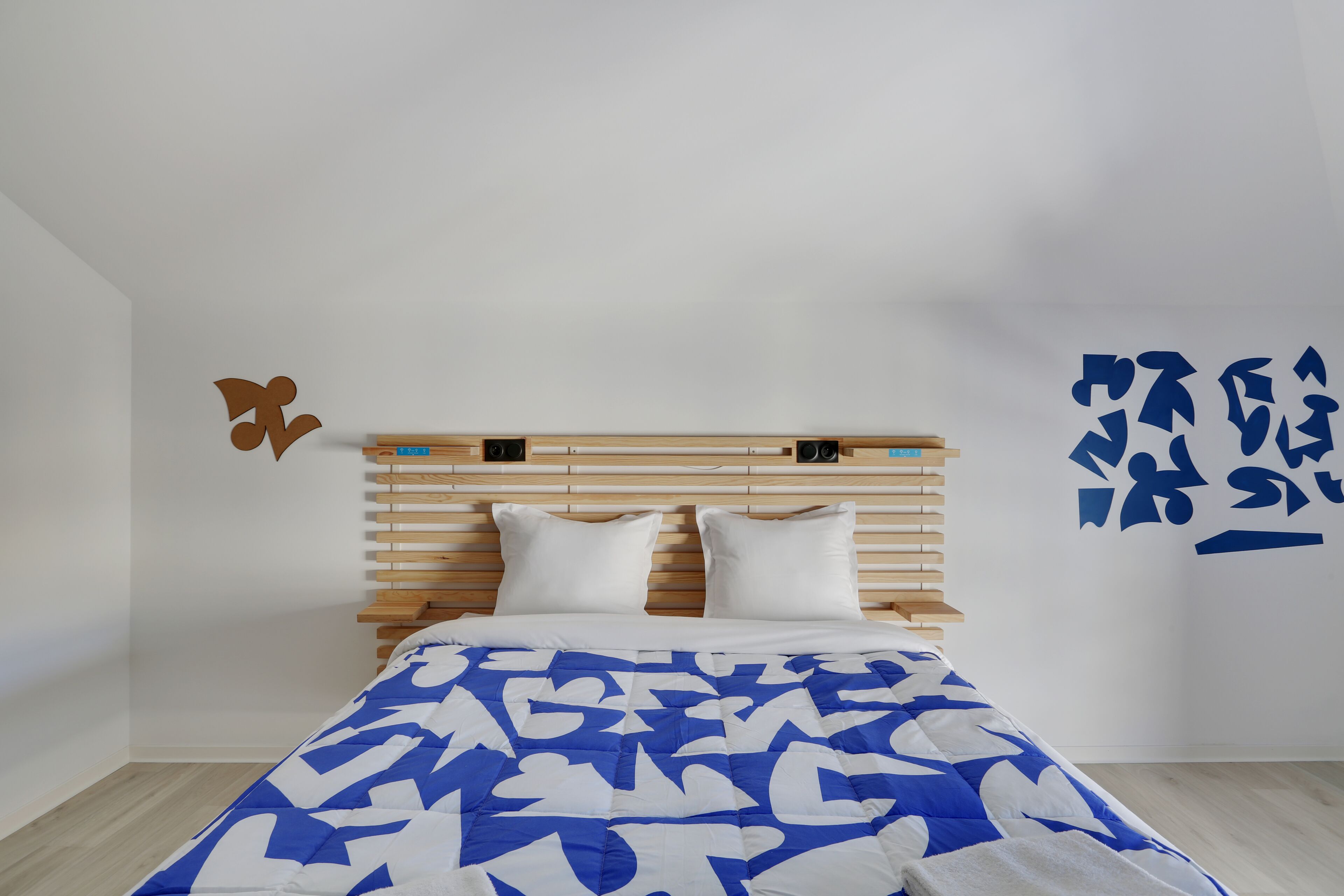 A bedroom with a wooden headboard, white bedding, and a blue and white patterned bedspread.