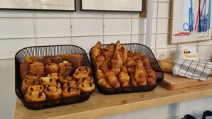 Two black baskets filled with pastries on a wooden counter, with a loaf of bread and a sign reading "NO PAIN NO TARTINE" in the background. - The People - Marseille - Hostel (Marseille)