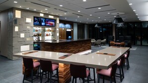 Un área de bar moderna con una barra larga, varios taburetes y una pantalla de televisión mostrando contenido.