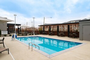 An outdoor swimming pool with lounge chairs and tables, surrounded by a fence and a wooden pergola. - Courtyard by Marriott Charlotte Steele Creek (Charlotte)