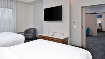 Et hotelværelse med to senge, et fladskærms-tv, et skrivebord med skuffer, en stol og en dør, der fører til et andet værelse.