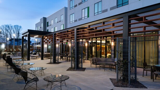 Un hotel moderno con mesas al aire libre, un porche cubierto y fachada de vidrio.