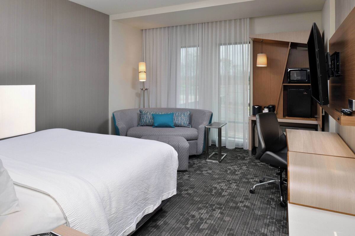 Een hotelkamer met een bed, een slaapbank, een bureau, een televisie en een klein tafeltje.
