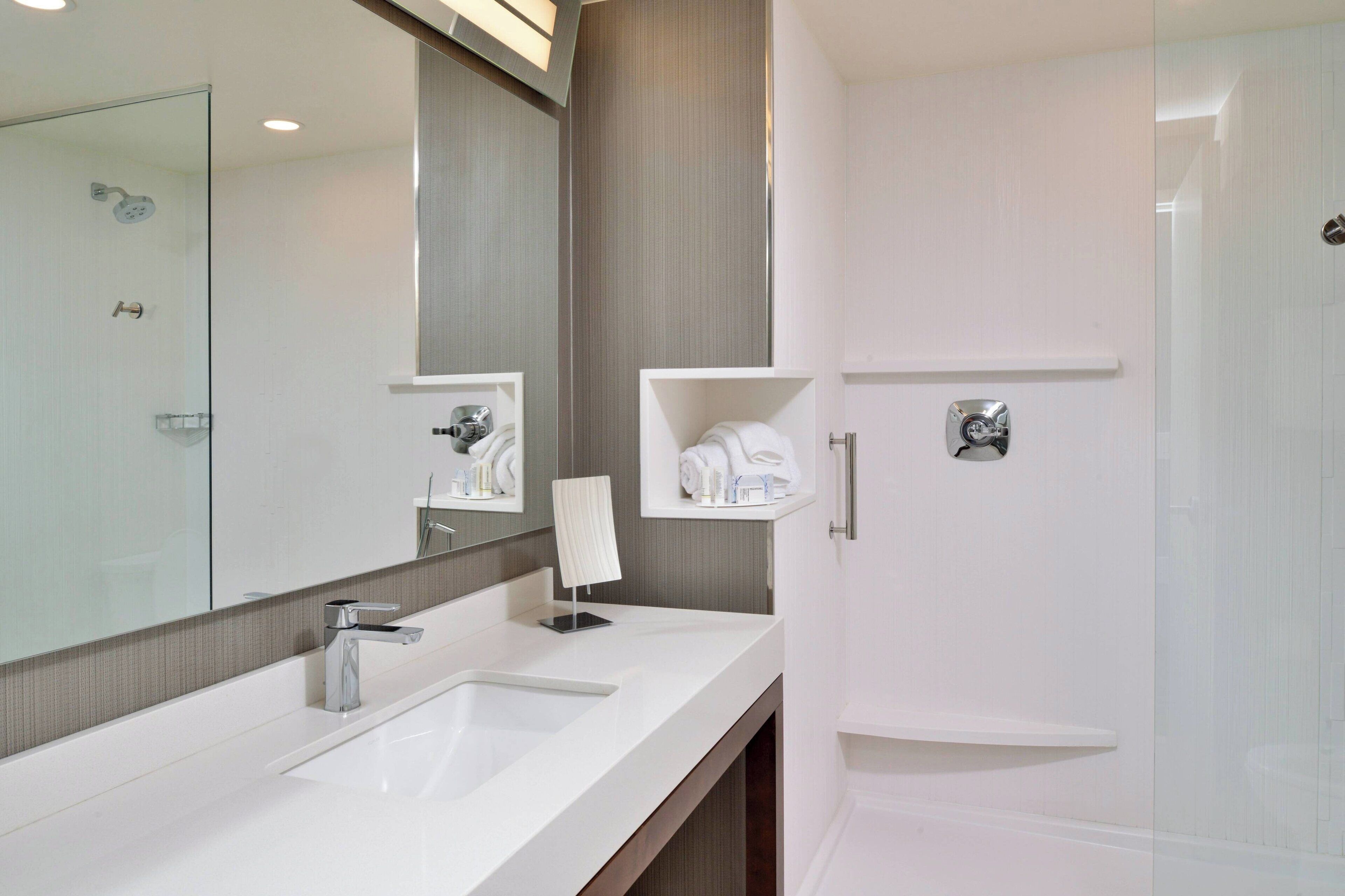 Un baño moderno con un espejo grande, un lavabo blanco, una ducha y un tendedero para toallas.