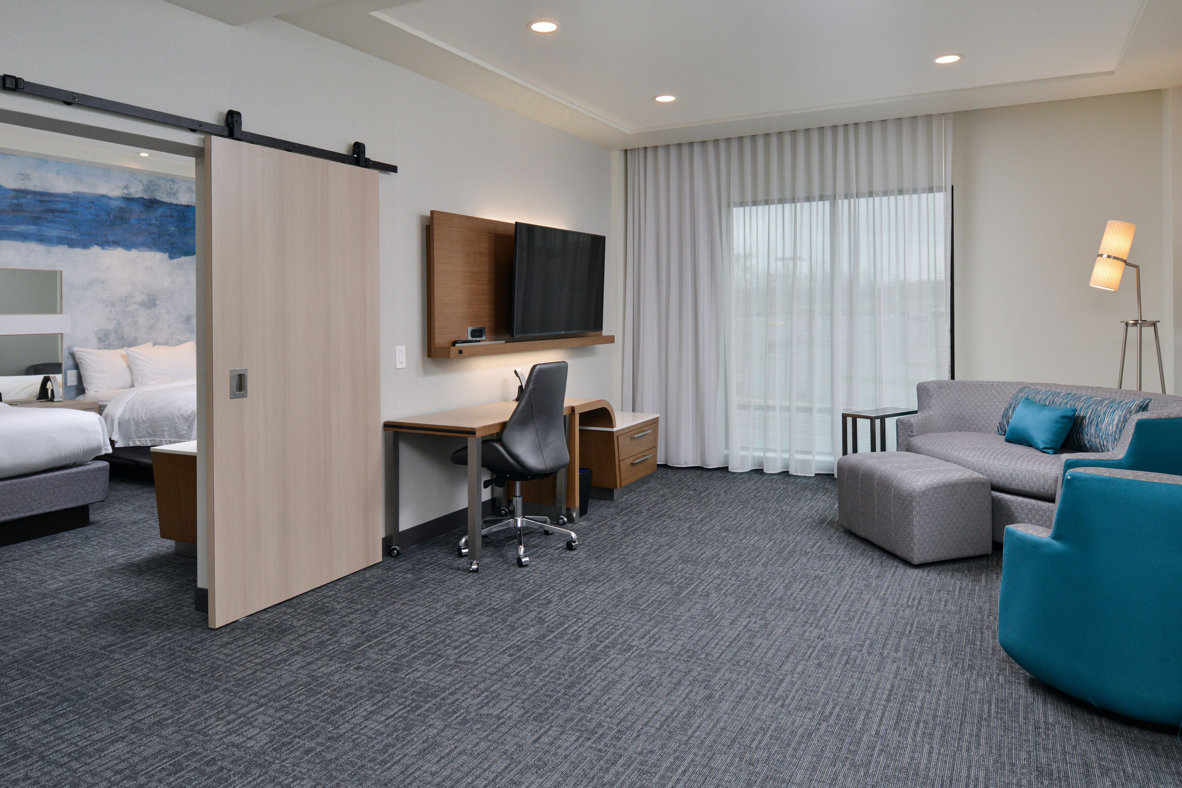 A hotel room with a bed, desk, chair, sofa, and a TV mounted on the wall.