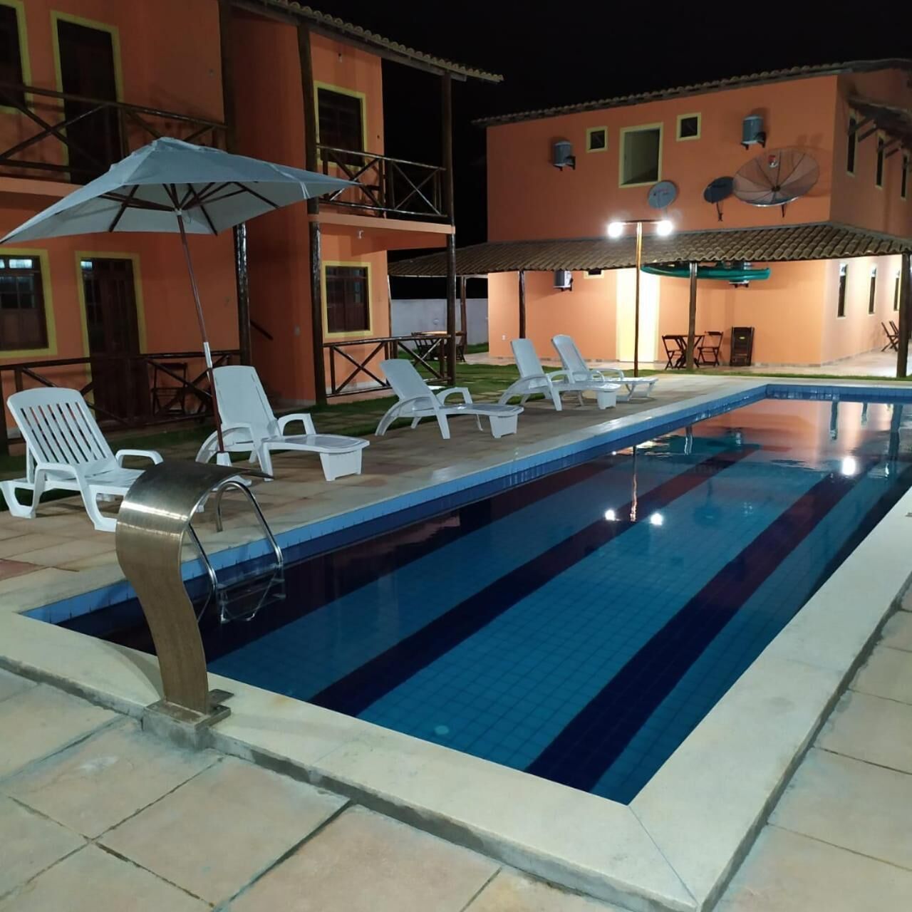 A swimming pool with lounge chairs and umbrellas, surrounded by a building with multiple windows and a tiled roof.
