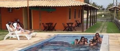 Una piscina con gente, un edificio con antenas parabólicas y palmeras al fondo.