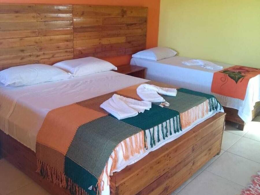 Une chambre avec deux lits, une tête de lit en bois, un sol carrelé et un climatiseur fixé au mur.
