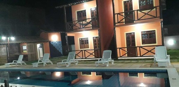 Un edificio de dos pisos con piscina, mobiliario exterior y una escalera.