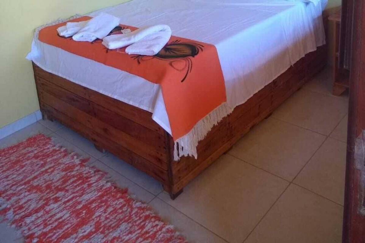 Una cama individual con cabecera de madera, ropa de cama blanca y una toalla roja y blanca en el reposapiés.