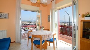A dining area with a round table and chairs, a view of the marina through glass doors, and a balcony with a railing.