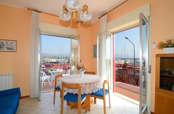 Un comedor con una mesa redonda y sillas, vista al puerto deportivo a través de puertas de vidrio y un balcón con barandilla.
