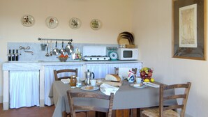 A rustic kitchen with a dining table set for four, surrounded by wooden chairs. - Podere Conti (Filattiera)
