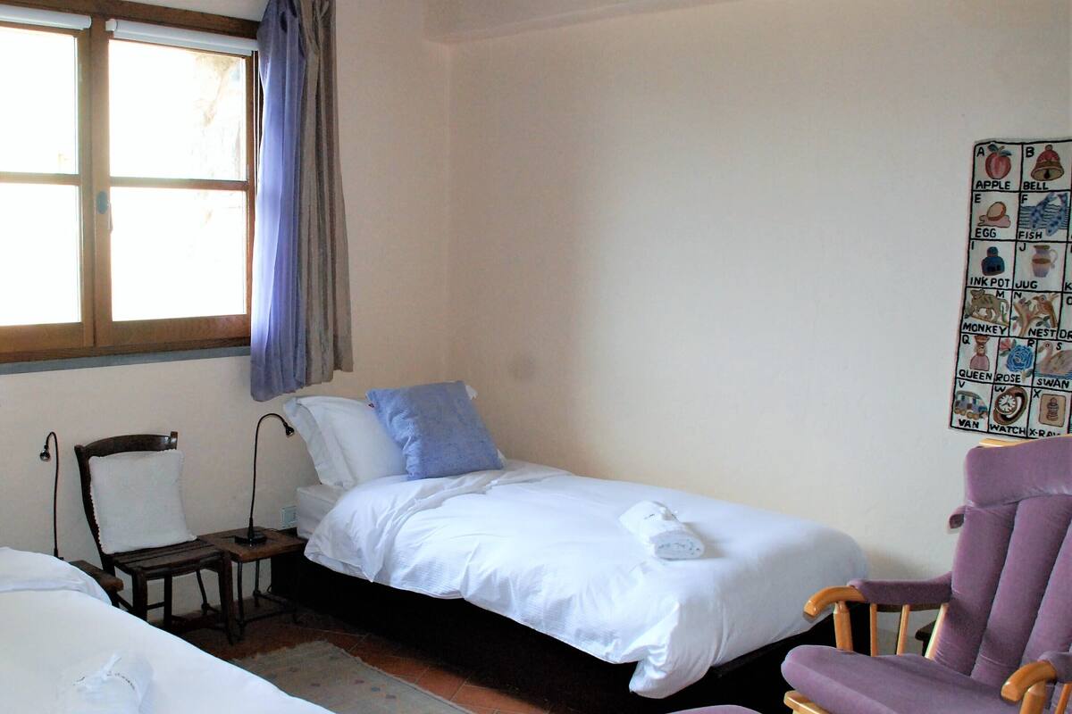 Una habitación pequeña y sencilla con una cama individual, una silla y un panel decorativo en la pared.