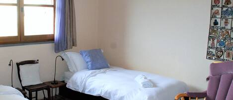 Une petite pièce simple, avec un lit simple, une chaise et un mur orné d’un tableau décoratif.